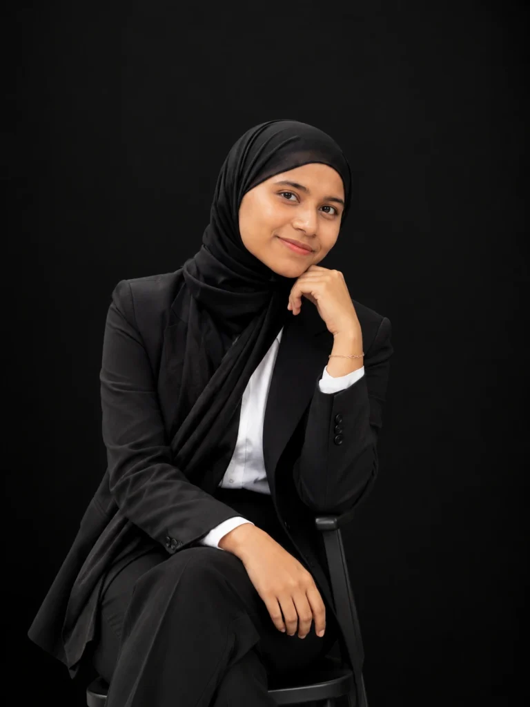 SEO-Optimized Image Alt Text: `Best digital marketer in Kerala – Fathima Shamna in a professional black suit and hijab, seated against a black background for her digital marketing portfolio.